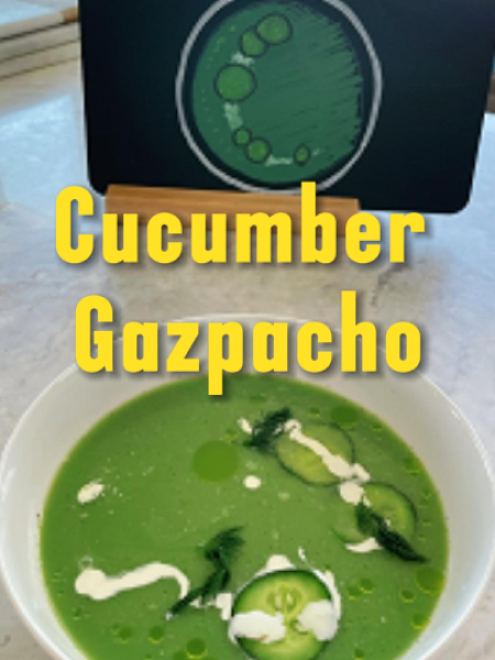 A vibrant green Cucumber Gazpacho served in a white bowl garnished with fresh dill, diced cucumber, and a drizzle of olive oil on a rustic wooden table.