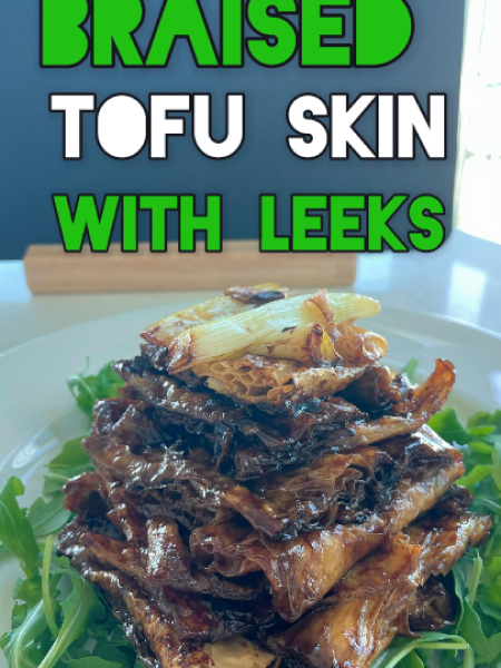Glossy braised tofu skin with leeks in a rich dark sauce, garnished with crispy fried leek greens, served in a ceramic bowl with chopsticks and steamed rice nearby.