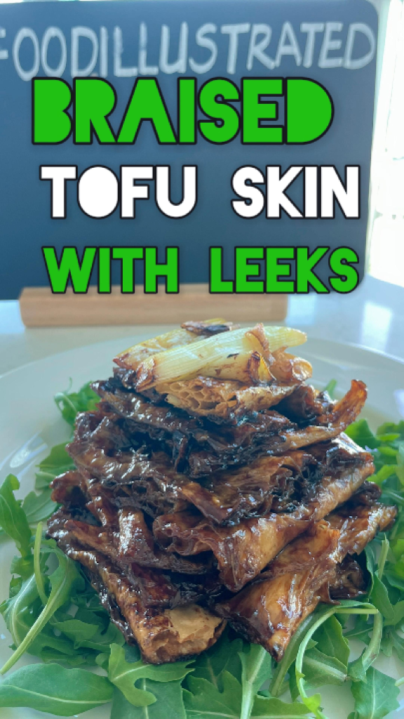 Glossy braised tofu skin with leeks in a rich dark sauce, garnished with crispy fried leek greens, served in a ceramic bowl with chopsticks and steamed rice nearby.