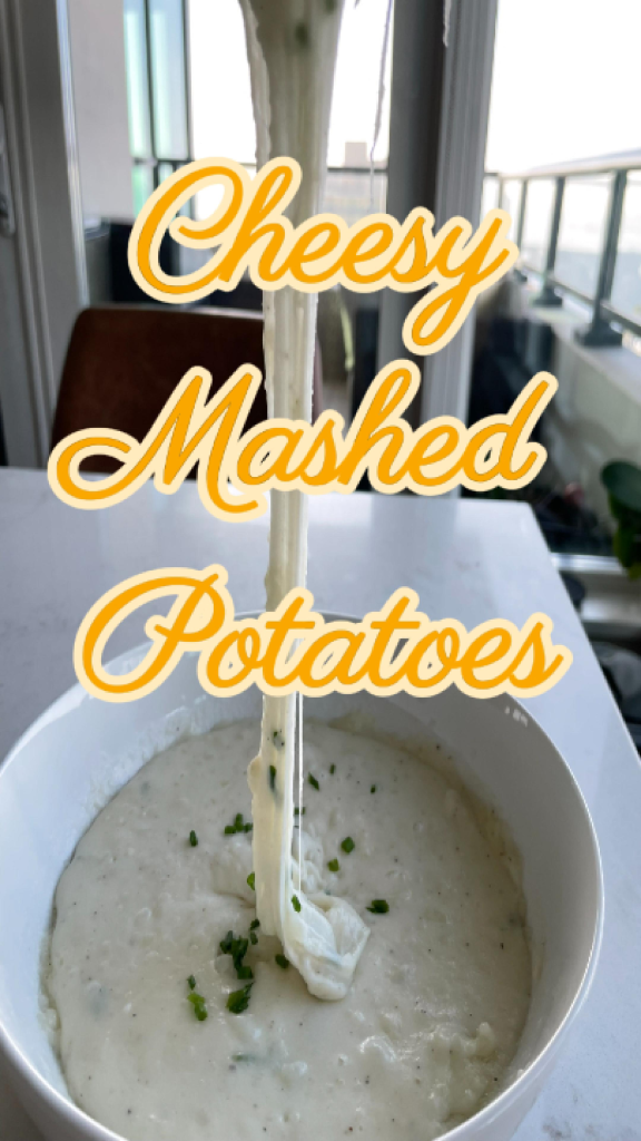 Close-up of a spoonful of creamy mozzarella mashed potatoes with long, stretchy cheese strands connecting the spoon to the bowl, garnished with chives.