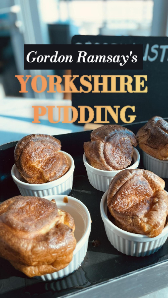 Tall, golden Yorkshire puddings baked in a muffin tin, crispy edges and fluffy centers, served on a wooden board with a small jug of gravy.