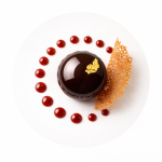 Chocolate cake slice with raspberries and mint on a white plate