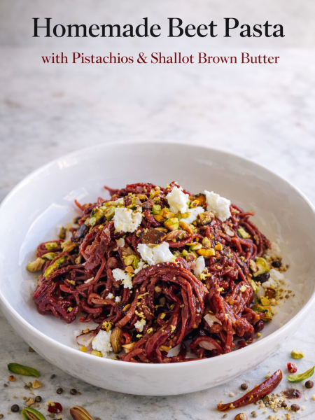 A bowl of vibrant homemade beet pasta with pistachios, tossed in brown butter sauce and topped with crumbled goat cheese