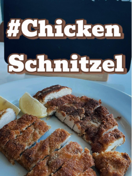 Golden brown crispy chicken schnitzel cutlets on a wire rack with lemon wedges and fresh parsley in a cast iron skillet.