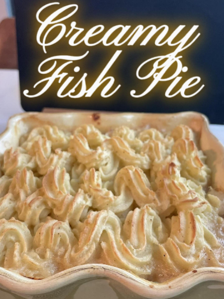 Golden brown Easy Creamy Fish Pie in a white baking dish served with a spoon, showing creamy filling with white fish, vegetables, and hard-boiled eggs.