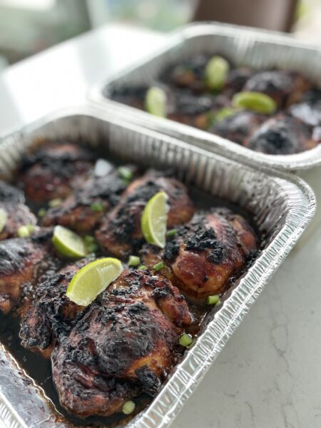 Large platter of party-size Jamaican jerk chicken thighs with charred, caramelized skin, garnished with
