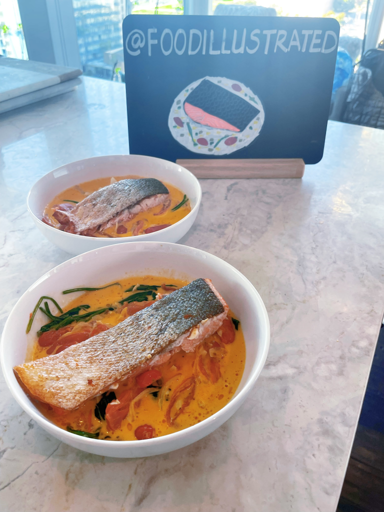 Creamy Tuscan salmon fillets in a white skillet with velvety garlic cream sauce, sun-dried tomatoes, and fresh spinach, ready to serve.