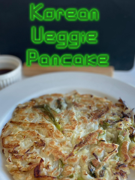 Crispy Korean vegetable pancake (yachaejeon) sliced into wedges on a wooden board with a small bowl of soy dipping sauce.