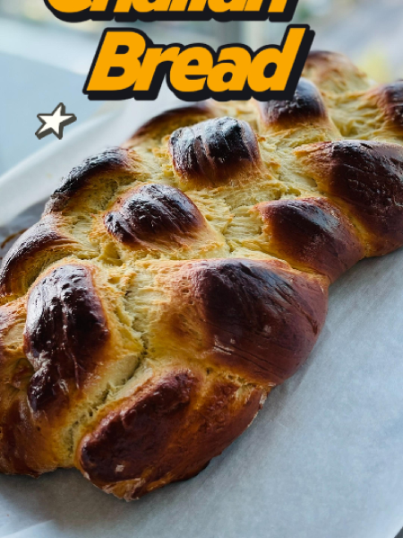 golden brown, braided homemade Challah bread loaves resting on a parchment-lined baking sheet, fresh out of the oven.