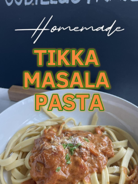 A creamy, pink-orange tikka masala pasta in a white bowl, topped with grilled chicken pieces, fresh cilantro, and a sprinkle of red chili flakes, showcasing the perfect Indian-Italian fusion dish.