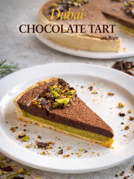 Whole Dubai Chocolate Tart on a serving platter with cocoa powder dusting, white chocolate drizzle, and roasted pistachio garnish